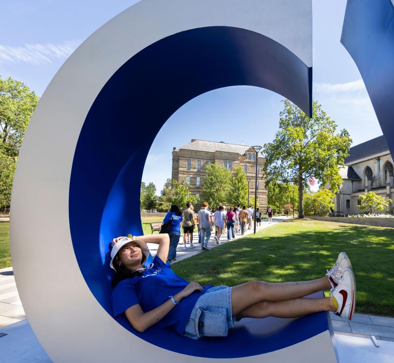 A student lounging in the letter “C” of the “CWRU” sign on campus.