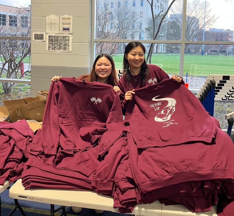 Two students holding up maroon sweatshirts inside Veale Recreation Center.