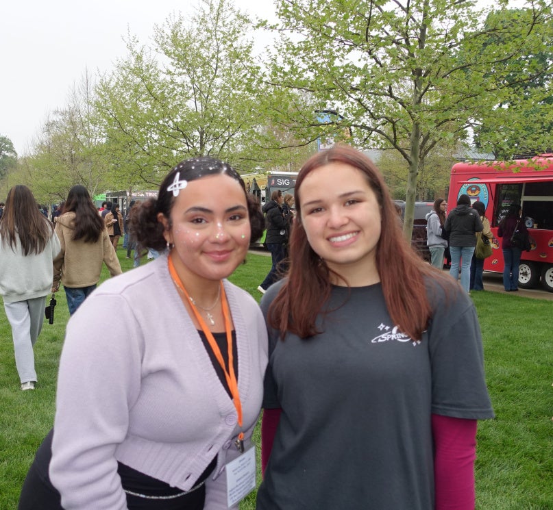 Two students pose on East Bell Commons with a stage and food trucks in the background.