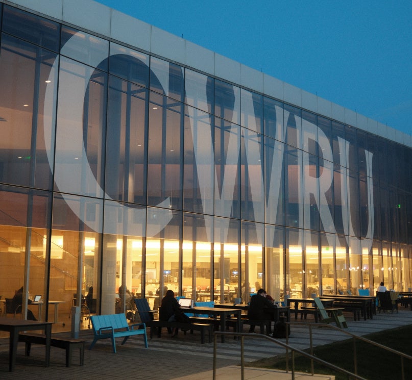 Large "CWRU" lettering on the side of Tinkham Veale University Center glows at dusk as students study inside.