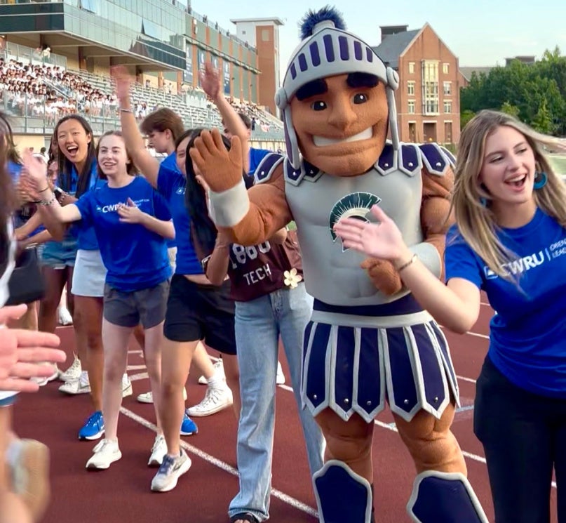 CWRU mascot Spartie in a line of high-fiving students on DiSanto Field during orientation.