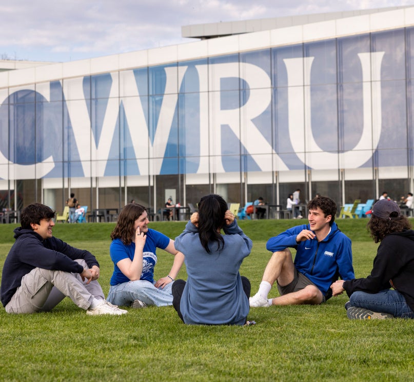 Five students sit in front of large “CWRU” signage on Freiberger Field.