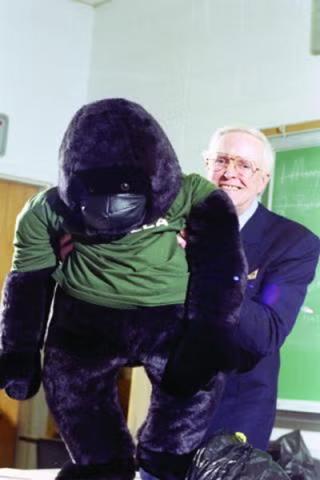 Richard L. “Gorilla” Osborne holds a stuffed toy gorilla in a classroom while wearing formal attire