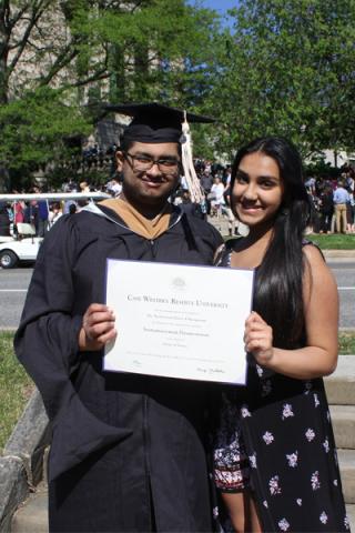 Two people smiling holding a degree; one is wearing graduation robe and cap