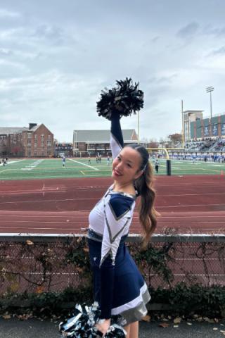 Nursing student Alicia Lee cheers with pom poms at a sporting event in the CWRU stadium.