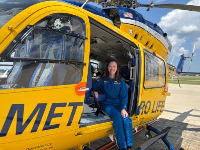 Amanda Rowe in a blue jumpsuit sits inside a yellow helicopter.