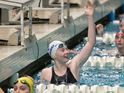 Claire Kozma raises hand in pool during a swim meet. 