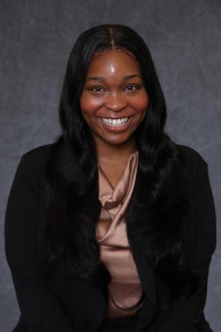 Miriam Ashford in pink blouse and black jacket poses in front of grey background