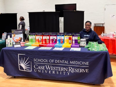 A woman sits at a table with a CWRU banner and a display of different products.