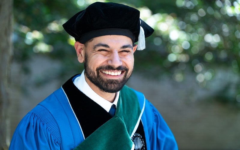 A male student smiling at the camera in graduate regalia
