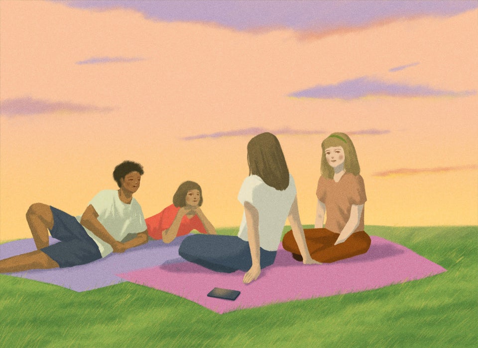 An illustration of four people sitting together on blankets in a grassy field, chatting with each other, with one phone behind one person’s back.