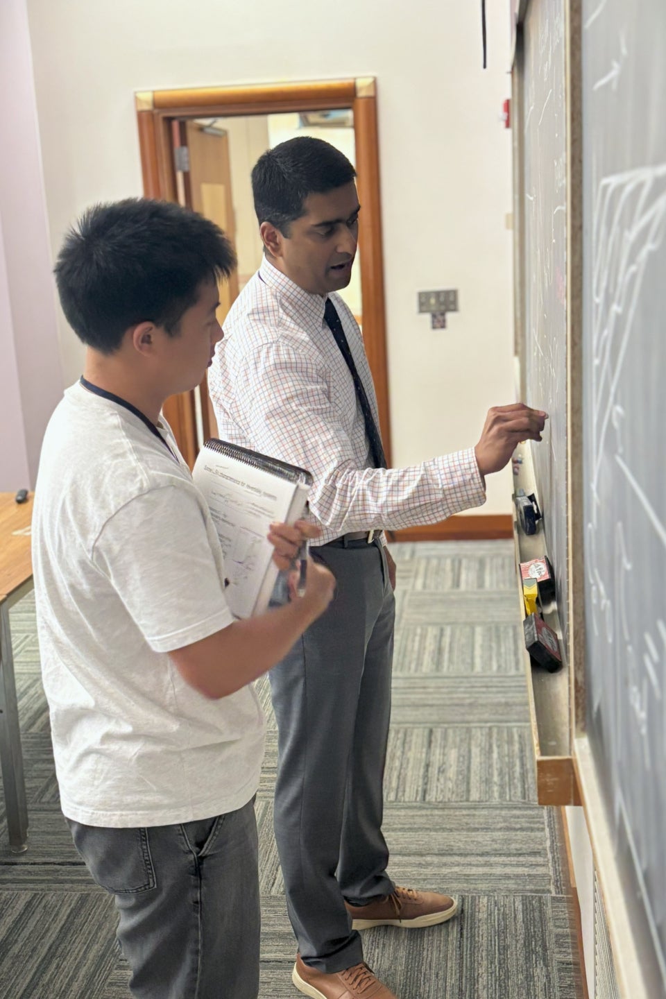 A faculty member and workshop participant have a discussion at the blackboard during a lecture.