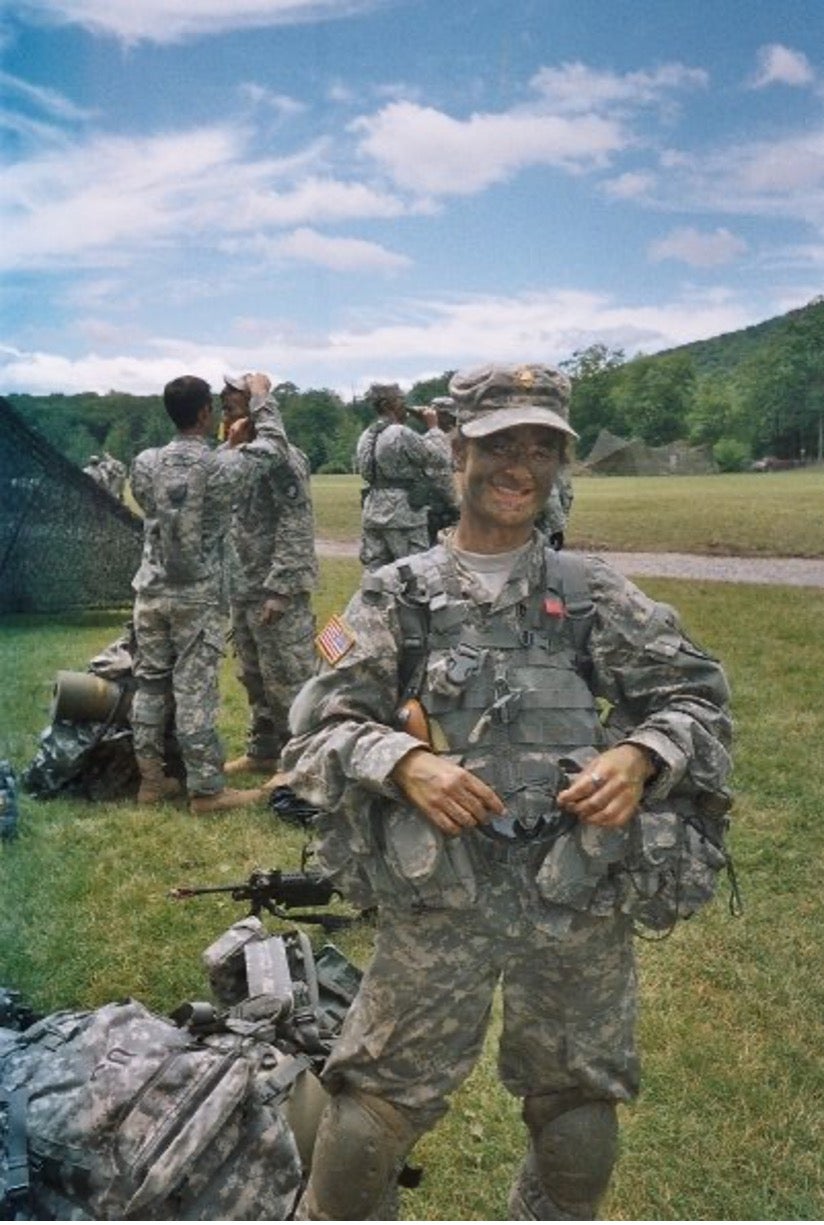 Major Bre Boswell stands in fatigues with other service members in the background..