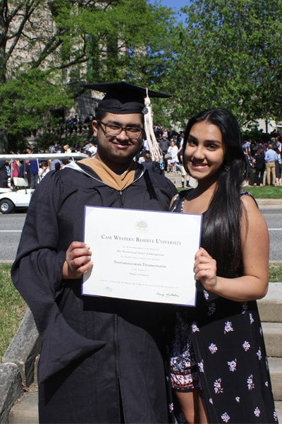Two people smiling holding a degree; one is wearing graduation robe and cap