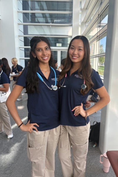 Nursing student Alicia Lee poses with a classmate in their scrubs in an atrium.
