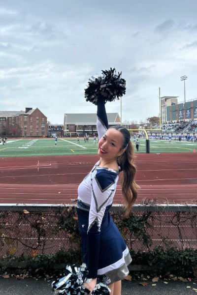 Nursing student Alicia Lee cheers with pom poms at a sporting event in the CWRU stadium.