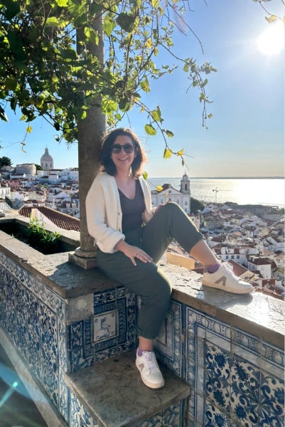 CRNA student Erin Tansey sits on a wall in front of a tree and water.