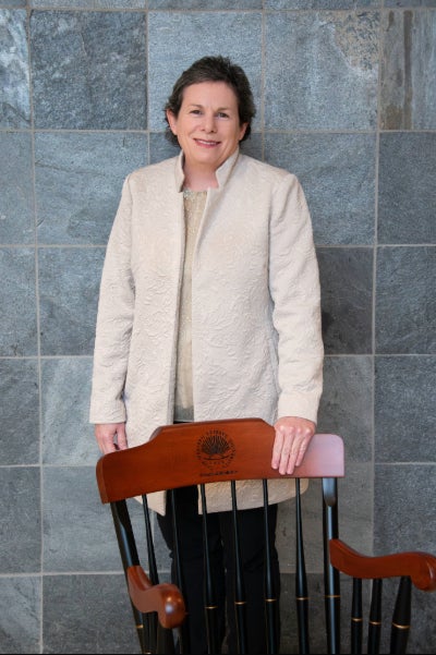 Susann Brady-Kalnay, PhD, pases in a white jacket behind a brown chair.