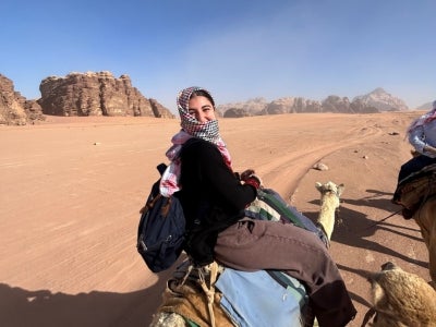 Catherine Esper rides a camel in the desert. 
