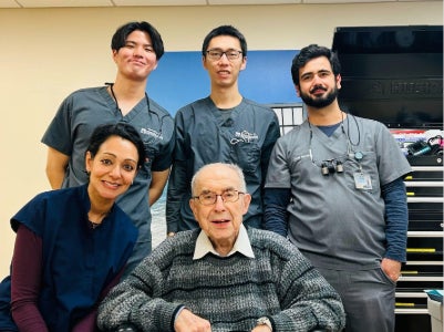 Three dental students and faculty member Dr. Mahalaha pose with a seated geriatric patient.