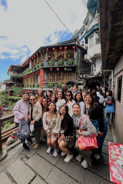 A group of nursing students poses in front of a mountain building in Taiwan with blue skies behind