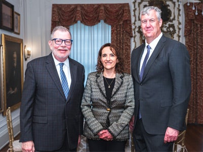 Three people in formal attire stand in a well-decorated room smiling at the camera.