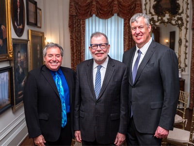 Three men in suits stand together and smile at the camera