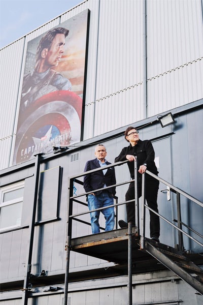 Two people stand on a metal platform outside a building with a large "Captain America" poster.