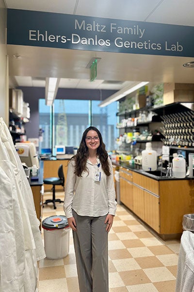 Chloe Meyer poses for a photo at the entryway of the Maltz Family Ehlers-Danlos Getics Lab