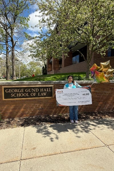Dalerys Feliciano Acevedo standing in front of the Gund School of Law sign with a large check and ballons