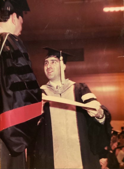 John Damiano receiving his diploma wearing a cap and gown