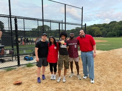 Five people posing in front of a baseball dugout