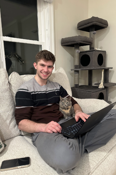 Jacob Hoffa sits on the couch with his laptop and cat.
