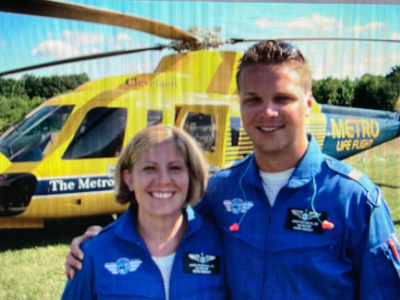 A man and woman dressed in blue stand in front of a yellow helicopter.