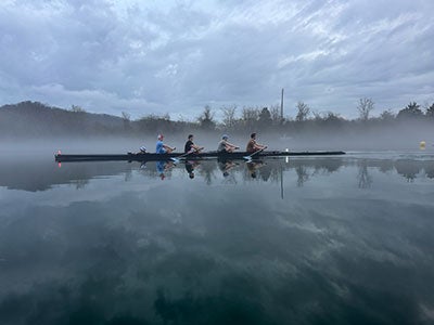Photo of members of the CWRU Crew in their boat moving through the water in on a foggy morning