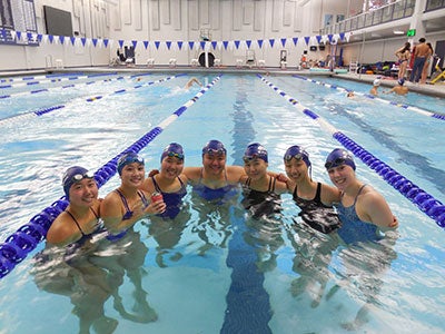 Seven women swimmers pose for a photo in a semi-circle in the pool in Veale Center