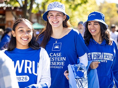 Three students walk on campus smiling as they wear CWRU blue gear