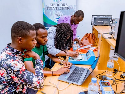 Students at Kibogora Polytechnic collaboratively work with laptops and electronics on a lab bench, focused on a hands-on technology lesson.