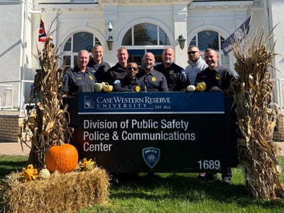 Photo of members of the CWRU PD posing for a photo in front of building sign surrounded by fall decor