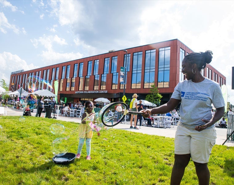 Photo of a child and adult  joyfully playing with bubbles in front of the Midtown Collaboration Center building.