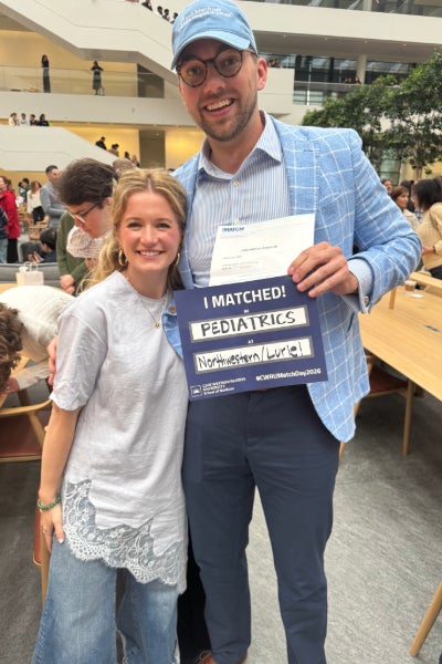 Brian Bangs smiling with a woman while holding a sign that reads "I matched in pediatrics at Northwester"
