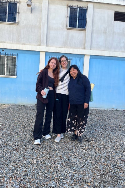 Three women stand in front of a blue wall.