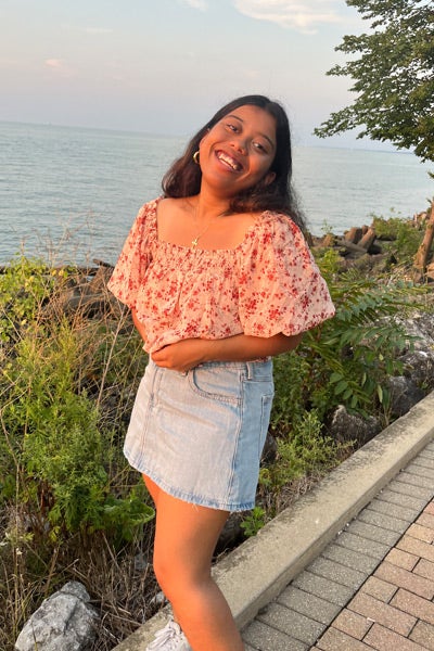 Jennifer G. D’Silva smiles at the camera with a beach scene in the background