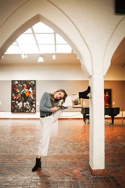 Graduate dance student Baylee Van Patten stretches with one leg braced against an archway