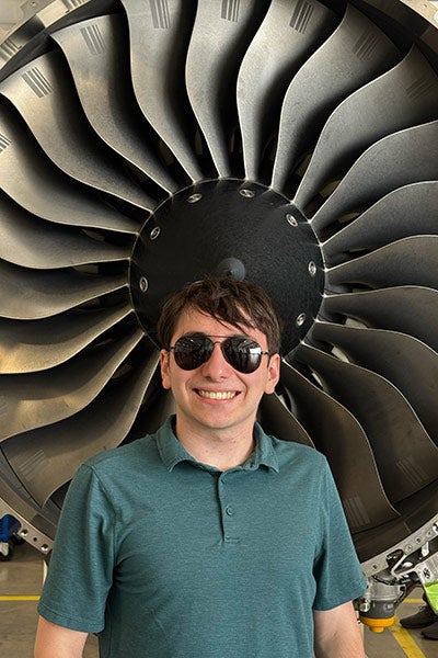 David Kaplan poses for a photo in front of the blades of a jet engine