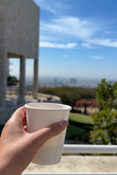 A hand holds up a coffee cup with a vista of Los Angeles in the background