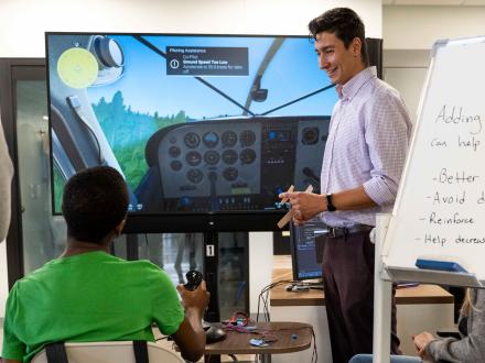 Photo of a PhD leading a demonstration of an aviation haptics program for a high school student