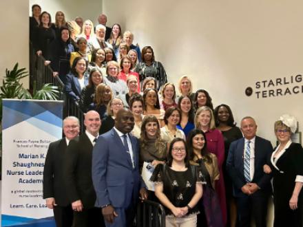 A large group of people poses on a staircase by a sign for the arian K. Shaughnessy Nurse Leadership Academy. 