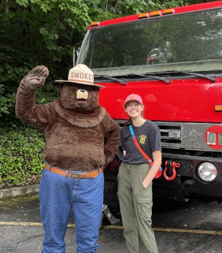 Meg Corley standing with Smokey the bear in front of a truck