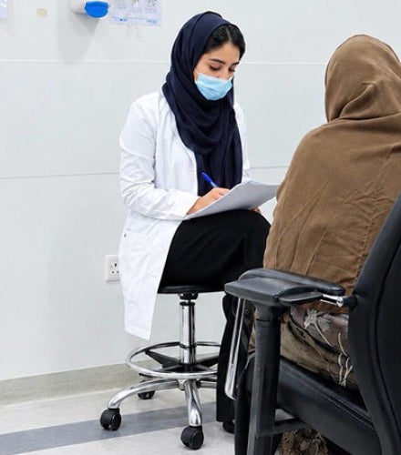 Rania Aljohani speaks with a patient and takes notes with the patient's back to the camera